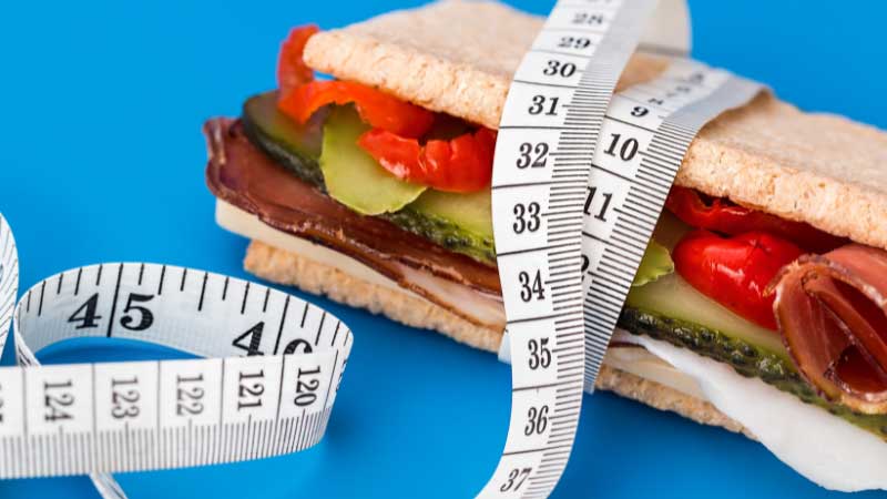 Calcolo fabbisogno calorico 4 Panino avvolto da un metro da sarto, simbolo di dieta e controllo delle porzioni